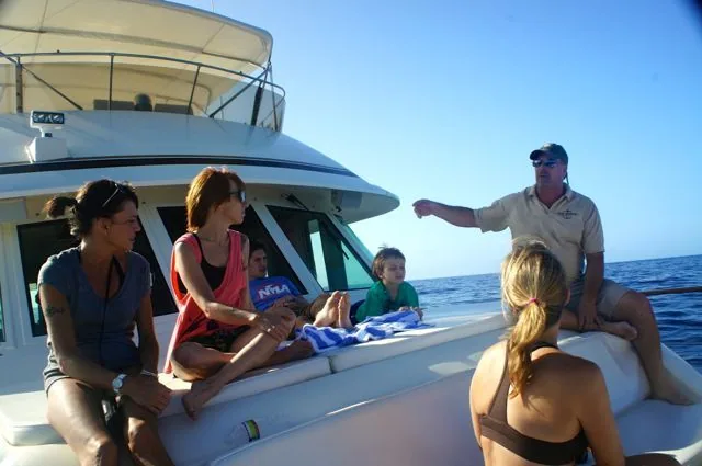 A group of people sitting on a boat with a man pointing