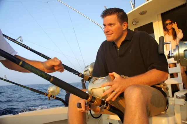 A man is sitting on a boat holding a fishing rod