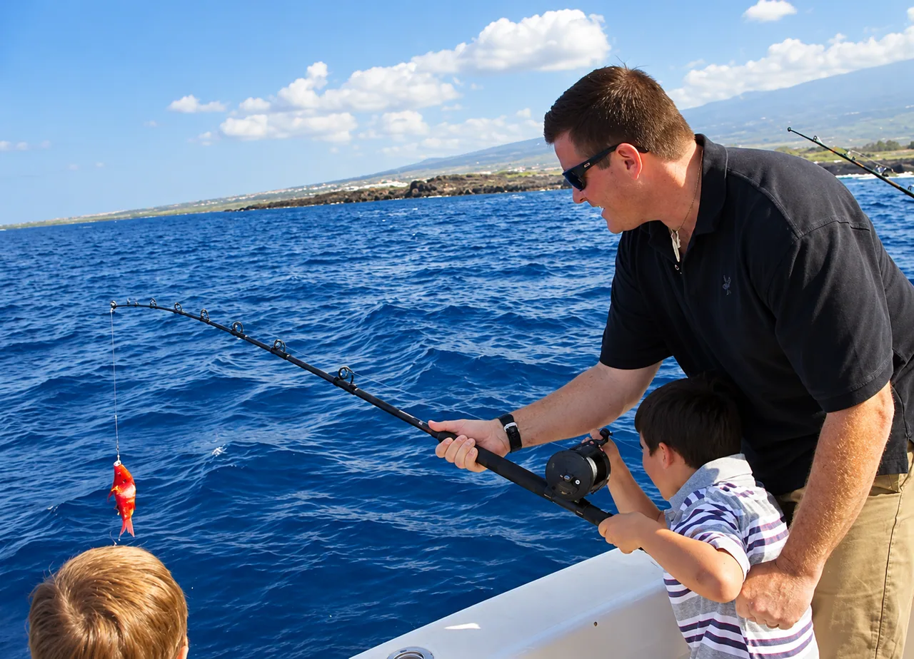 Adult helping a child fish with a rod and reel off the Kona coast