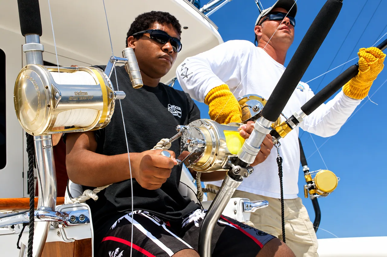Angler and crew member handling fishing rods and reels aboard a Kona charter boat